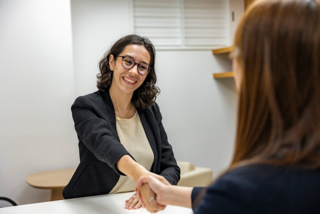 Two adults seated at a table in a bright office, one asking a question while the other listens attentively.