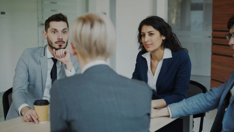 Employees review schedules together at a bright workplace table while a supervisor listens.